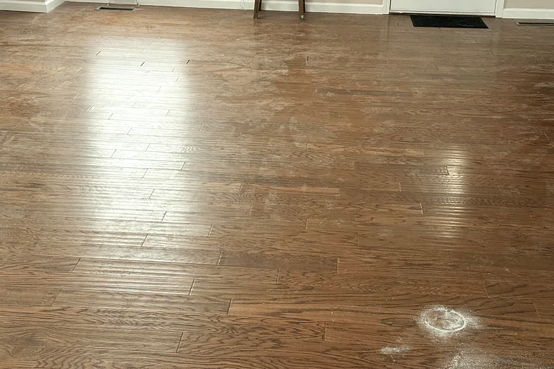 A hardwood floor before cleaning: a film of dust and white residue dulling the boards