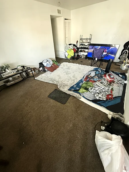 An apartment living room before a move-out clean: belongings, trash and debris across the carpet