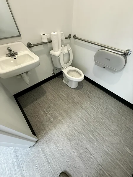 The same office restroom after a post-construction clean: clean toilet, sink and grab bar, floor mopped and the room restocked