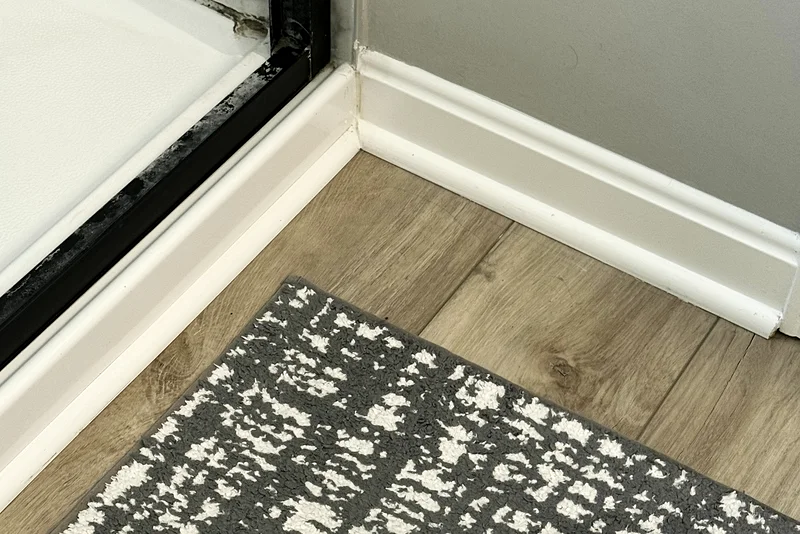 The same shower door track after cleaning: clean frame, clear track and a fresh bath rug