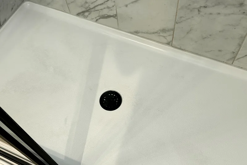 The same shower tray after cleaning: bright white, clear drain
