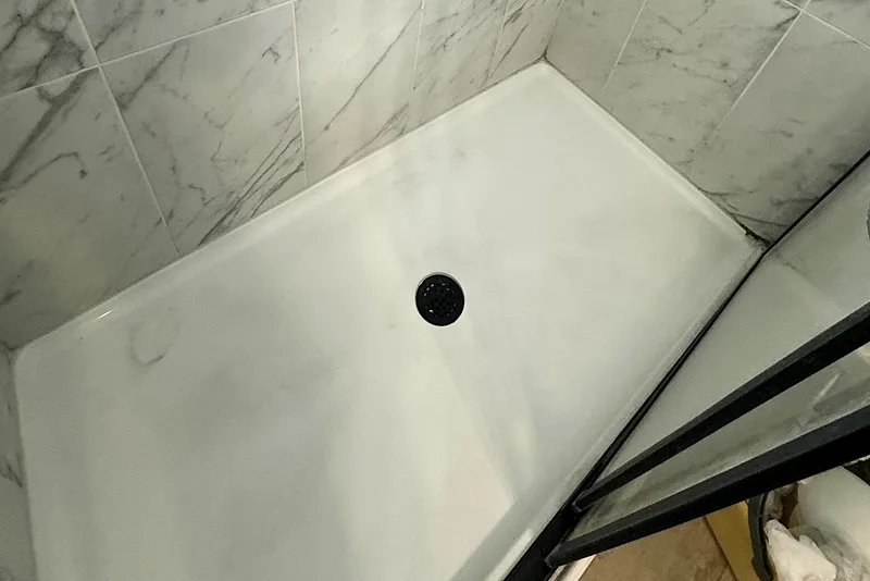Marble shower with a dirty acrylic tray and drain before cleaning