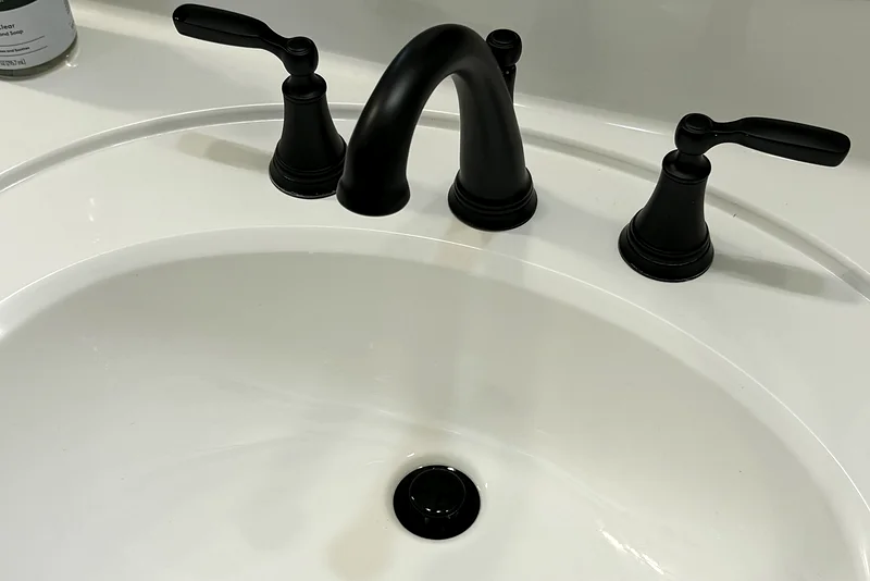 The same bathroom sink after a deep clean: spotless white basin and a polished black faucet