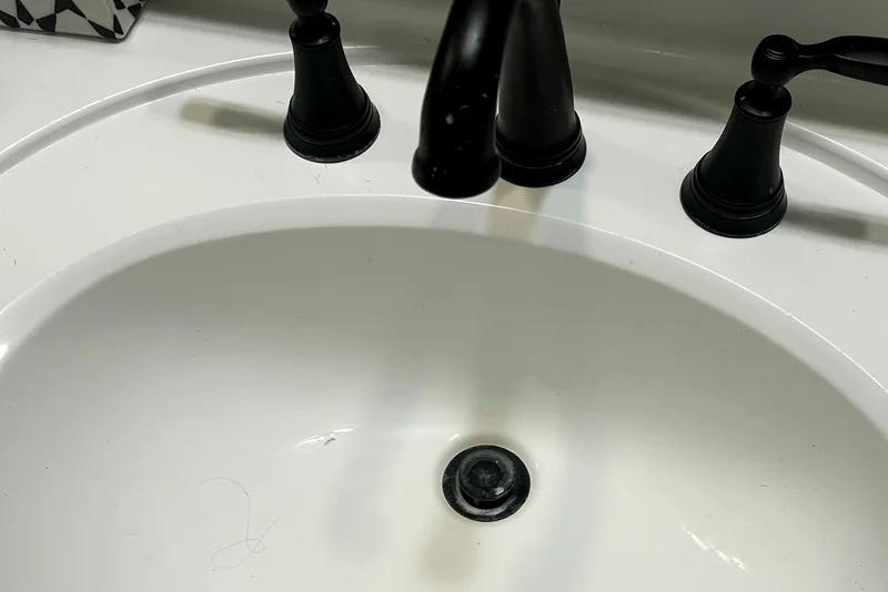 A bathroom sink with a black faucet before cleaning: staining around the basin and blue toothpaste smears