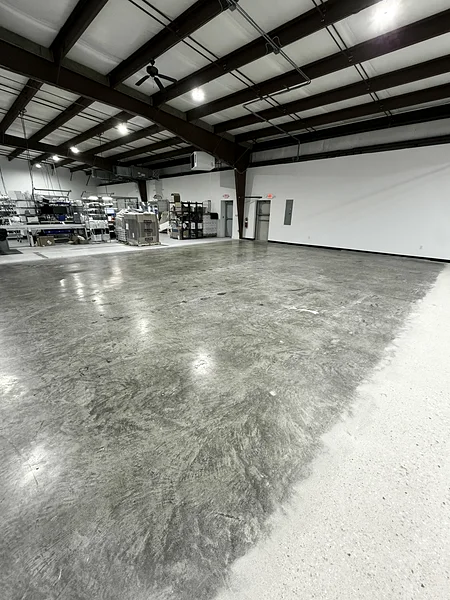 The same warehouse concrete floor after scrubbing and polishing, reflecting the lights overhead