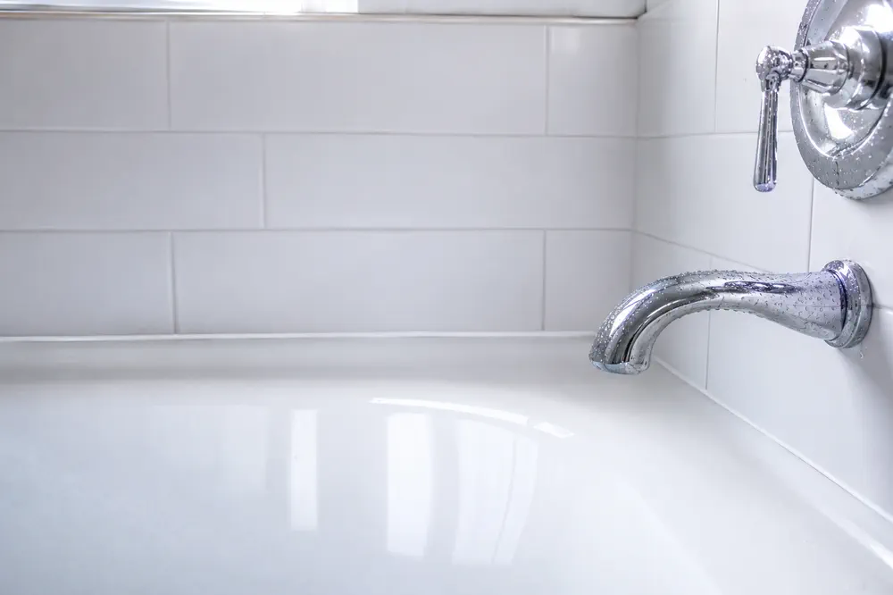 A spotless white tiled bathtub and chrome fixture after a deep clean