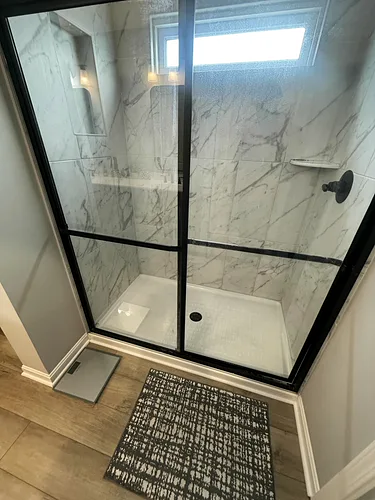 A marble shower with a black-framed glass door, cleaned and streak-free