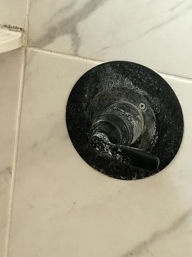 A close-up of a dirty shower valve with soap scum and water spotting, before cleaning