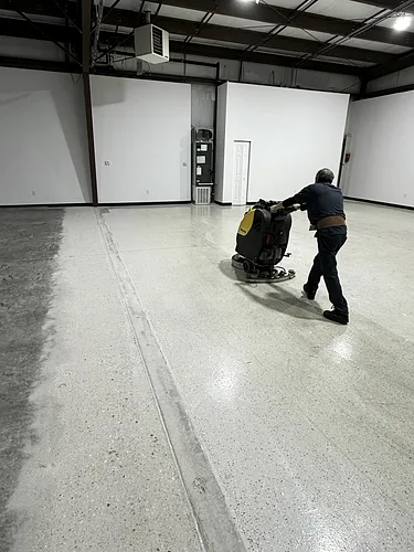 A Jmar crew member running a walk-behind floor scrubber across the warehouse concrete